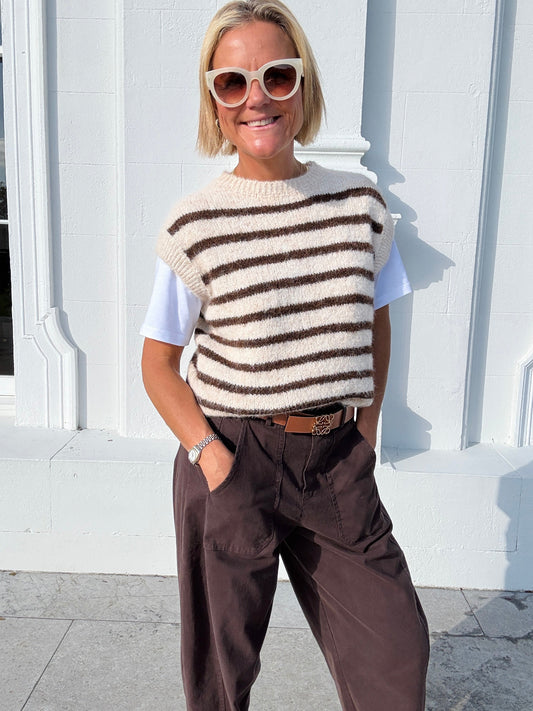 Amy wearing a striped sweater vest and sunglasses standing against a white building.
